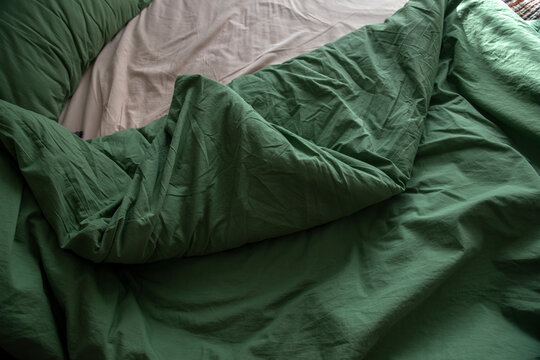 An unassembled bed in the bedroom, a blanket, and green and beige bedding.