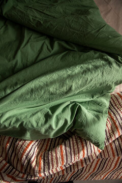 An unassembled bed in the bedroom, a blanket, and green and beige bedding.