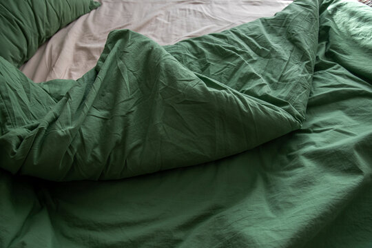 An unassembled bed in the bedroom, a blanket, and green and beige bedding.