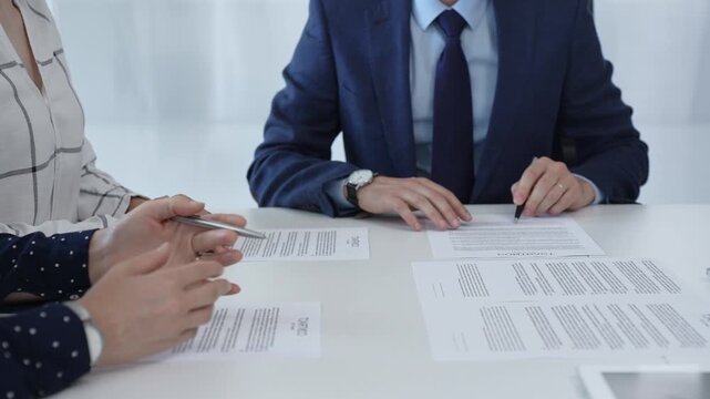 Business people analyzing contract details, gesturing with pens and hands while discussing legal terms during collaborative meeting, focused on negotiation process