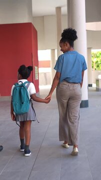 Black mother and her young daughter holding hands and walking together to school. Back to school concept with a child in uniform
