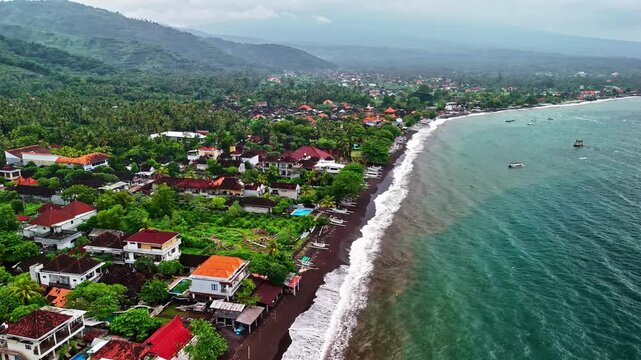 Aerial view of Amed Beach with its distinctive black volcanic sand, traditional outrigger boats, lush tropical vegetation, and coastal villas in Bali, Indonesia.