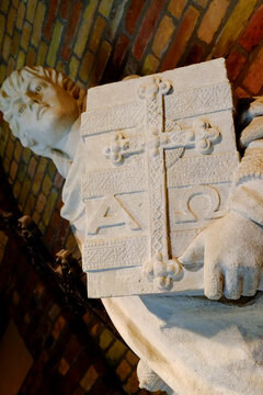 Carved stone figure holding a book with cross and alpha omega symbol