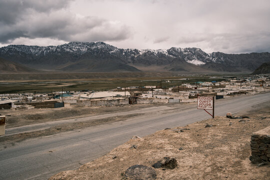 View of the Pamir Mountains rising above the town of Jirgatol with a guest house sign along the roadside in Jirgatol, Gorno-Badakhshan Auto, Tajikistan.