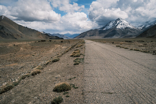 View of the Pamir Mountains rising above an arid landscape with a gravel road stretching into the distance in Jirgatol, Gorno-Badakhshan Auto, Tajikistan.