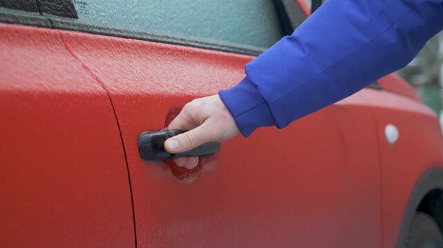 Driver's hand pulls the red car door handle but it doesn't open. Extreme weather conditions. Glaze ice