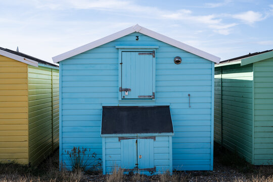 Blue beach hut with white trim and shuttered doors in a row of colorful seaside huts