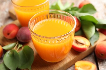 Glasses of tasty apricot juice, fresh fruits and leaves on wooden table, closeup © New Africa