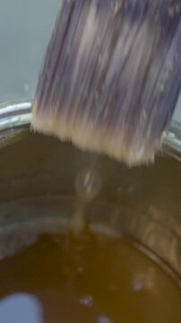 Craftsman wearing gloves immerses brush into varnish can. Bristles absorb finish, ensuring controlled application on wooden surface for protection and shine