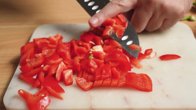 Hand dicing a red bell pepper on a marble cutting board