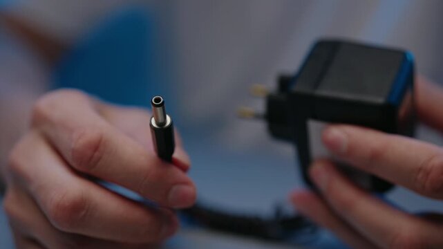 Close-up cropped shot of male hands holding black power adapter with European plug and DC barrel jack connector. Concept of electricity, energy, charging and technology. Shooting in slow motion.