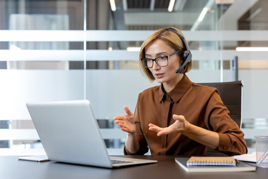 Businesswoman having a professional virtual meeting or online conference, communicating with clients or colleagues while wearing a headset and gesturing with her hands in an office environment