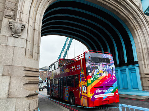 Colorful London double decker tour bus passing under Tower Bridge arch with vibrant advertising and open top sightseeing in London UK