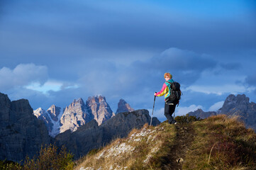 Fototapeta premium Solo female trekker reaches scenic ridge beneath dramatic storm clouds in Dolomites, Italy, symbolizing achievement, resilience, freedom, remote exploration and connection with wild alpine nature.