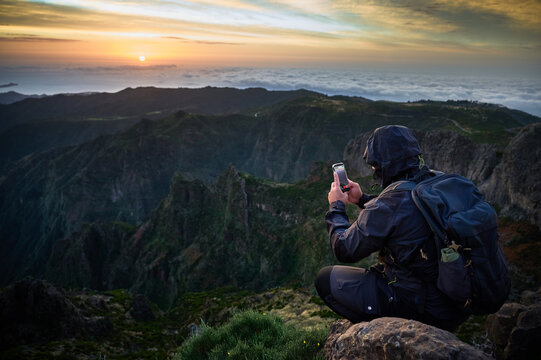 Backpacker films sunrise from Pico do Arieiro rocks, overlooking cloud sea, rugged peaks, valley cliffs, adventure travel and mountain content creation
