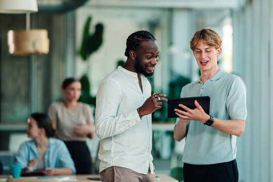 Diverse business professionals collaborating on a digital tablet, discussing ideas in a modern office environment
