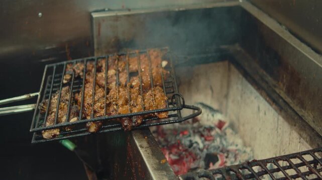 Cook brushes marinade onto skewered meat grilling over hot charcoal in kitchen