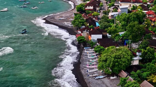 Aerial view of Amed Beach with traditional fishing boats resting on the black sand shore, surrounded by lush tropical trees and coastal villas in Bali, Indonesia.