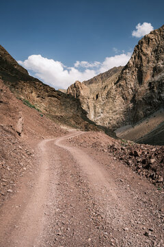 View of a winding dirt road through the rugged rocky landscape of the Bartang Valley under a clear blue sky in Chah Ab, Gorno-Badakhshan Auto, Tajikistan.