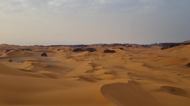 A vast, remote Saharan landscape stretches endlessly into the distance, covered in golden sand beneath a quiet, hazy sky. The barren Algerian desert conveys solitude, loneliness, isolation, remoteness