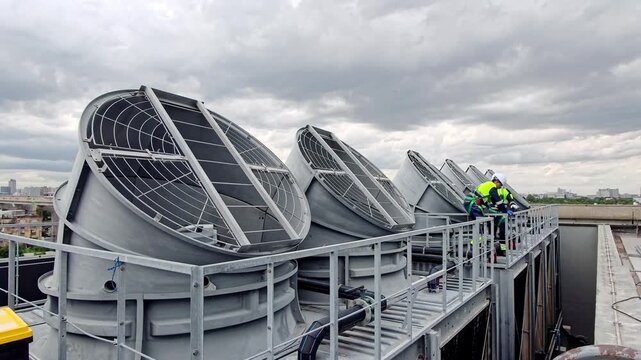 Technicians work on cooling units on a rooftop in an urban area