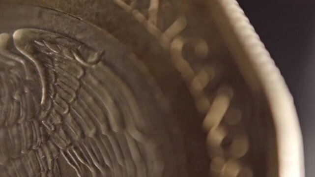 Macro close-up of a Mexican coin featuring the national eagle holding a snake in its beak and talon. The raised emblem and fine metallic texture are shown in detail