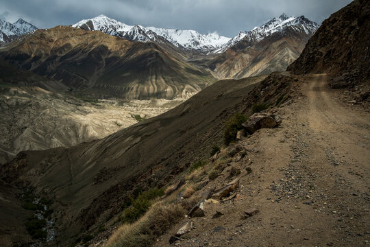 View of the rugged landscape of the Wakhan Corridor with a dirt road winding through the mountains under a dramatic sky in Badakhshan, Afghanistan.