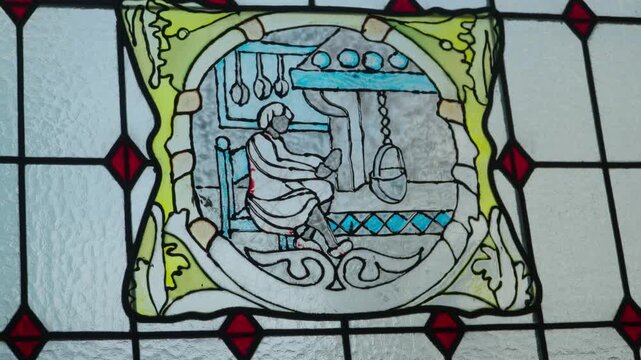 Detail of a stained glass window depicting an old artisan making cheese in Gijon, Asturias