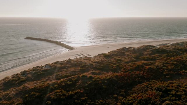 Aerial - Ofir shoreline with dune scrub stone groyne and sunlight glare on the ocean
