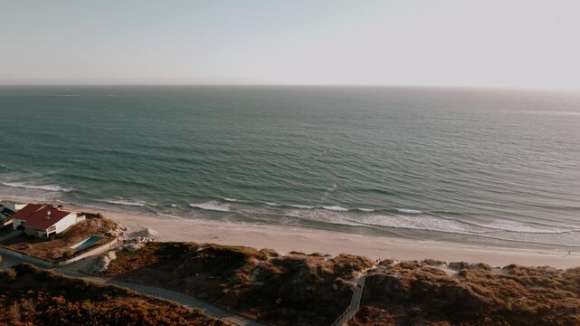 Aerial - kitesurfer on the Atlantic surf beside Ofir beach dunes and a shorefront house