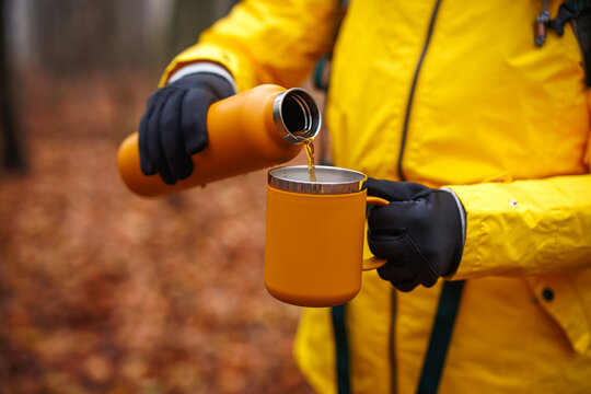 Refreshment during hiking outdoors. Female hiker pouring hot drink from thermos into travel mug in autumn forest
