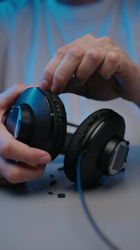 Close-up of hands holding old, broken headphones. Faux leather ear pads peeling and flaking off. Person removing damaged pads for repair, replacement. Concept of obsolescence and DIY repair.