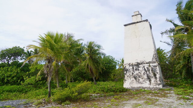 Scenic view of the unique, historic Tiputa Lighthouse constructed from coral stone and lime, standing on the edge of the lagoon pass among lush palm trees in Rangiroa, French Polynesia