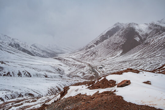 View of the snow-covered Kyzyl-Art Pass with a winding road cutting through the rugged mountain landscape under an overcast sky in Chah Ab, Gorno-Badakhshan, Tajikistan.