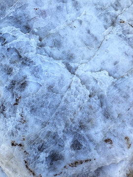 Detailed full frame macro shot of a raw quartzite or marble rock surface with crystalline structure, cracks, and subtle blue and brown veins