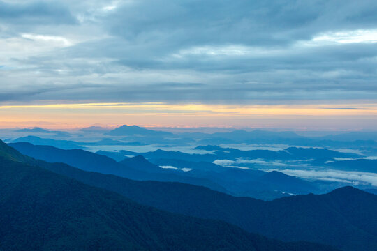 View of the Mardi Himal Trek mountain range at sunrise with layered silhouettes, mist-filled valleys, and a soft golden glow on the horizon in Pokhara, Gandaki Province, Nepal.