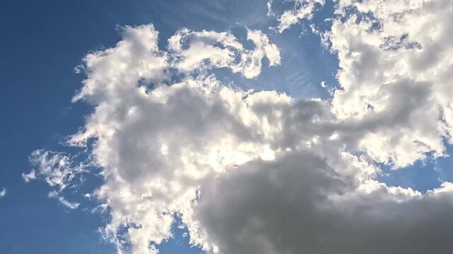 Fluffy white clouds slowly form a ring shape around an open patch of blue sky, drifting gently overhead with no birds present, captured outdoors in bright natural daylight.