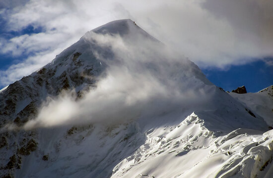 View of Diran Peak covered in snow with clouds drifting across the mountain face in Ganish, Pakistan.