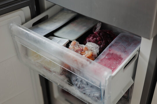 Open freezer drawer containing frozen food and meat stored in plastic bags, illustrating food storage, freezing, preservation and household kitchen organization.