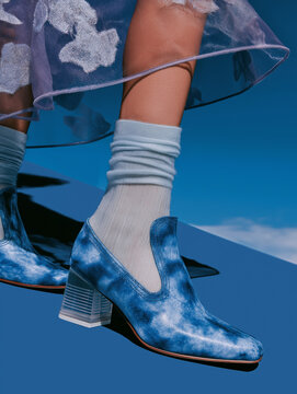 Blue suede ankle boot with slim heel is styled beside reflective metal. Ideal for premium shoe advertising, fashion catalogs, and modern editorial design.