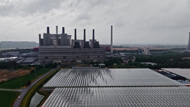 Aerial view of RWE Power AG Kraftwerk Neurath with industrial buildings and large greenhouses under a cloudy sky in Grevenbroich, Nordrhein-Westfalen, Germany.