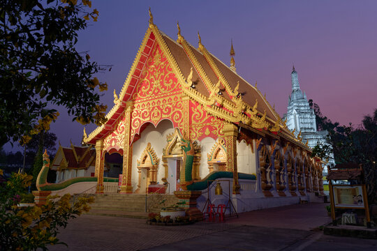 Wat Suan Tan temple beautifully illuminated at night, showing the golden assembly hall and the tall white chedi spire in the background.