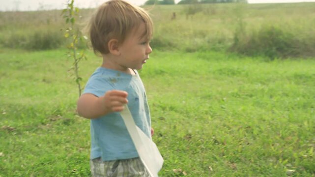 Toddler running and throwing paper airplane across garden with sibling nearby
