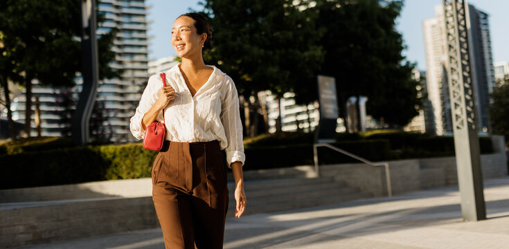 Korean woman enjoys a sunny stroll in a modern urban park setting