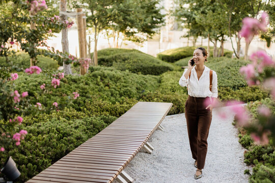 Korean woman enjoys a sunny day while talking on her phone in a serene garden