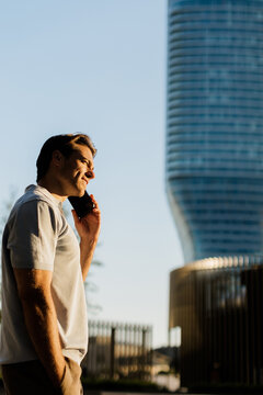 Smiling man talks on phone with modern building in background during sunset