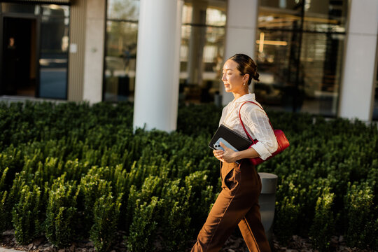 Korean woman walking confidently with a tablet and phone during golden hour