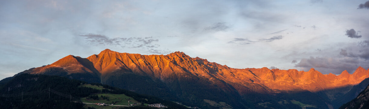 Panoramic Alpine Mountains Bathed in Golden Alpenglow Over Valley Village at Sunrise