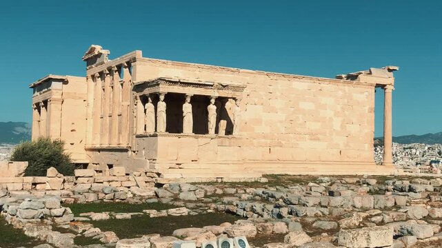 Scenic view of the ancient Erechtheion temple with the famous Caryatids on the Acropolis of Athens, Greece, with Mount Lycabettus and city panorama under a clear blue sky.

