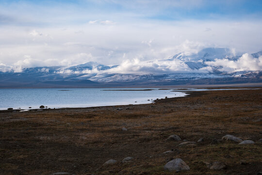 View of Karakul Lake with snow-capped mountains and rocky shores under a cloudy sky in Chah Ab, Gorno-Badakhshan Auto, Tajikistan.